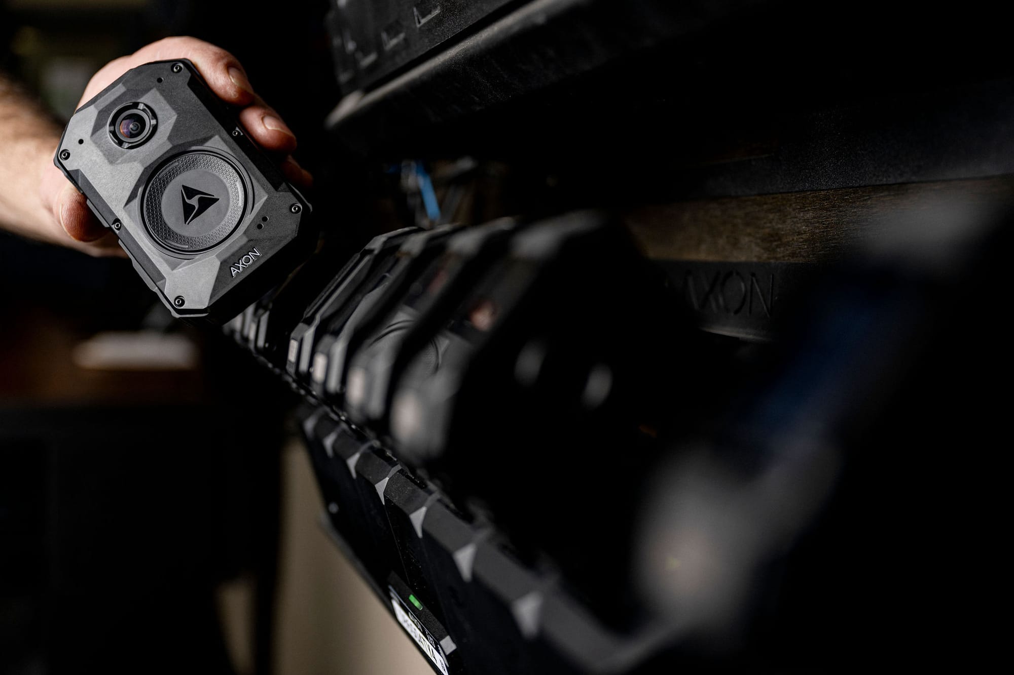 Hand grabbing an Axon body camera from a rack of them