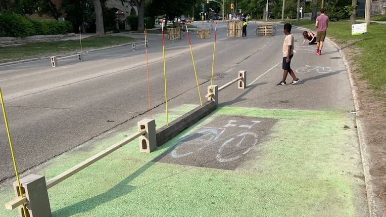 Horizontal photo of a DIY bike lane built on Wellington Crescent in early June. Several people are walking in it.